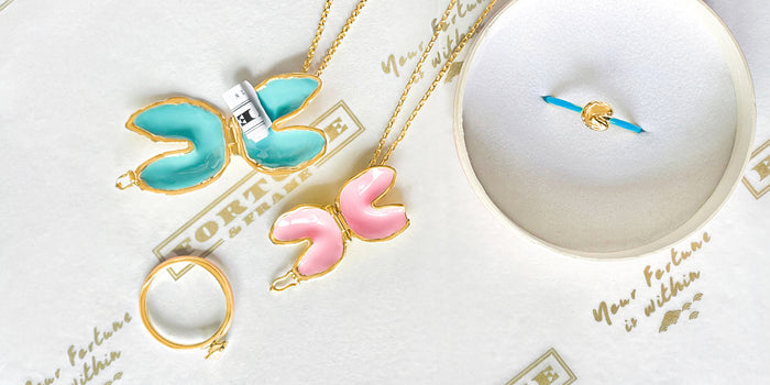 Aquamarine and Blush Fortune Cookie necklace along with Teal and Blush Fortune Cookie Rings. The aquamarine fortune cookie necklace is holding a rolled up fortune.